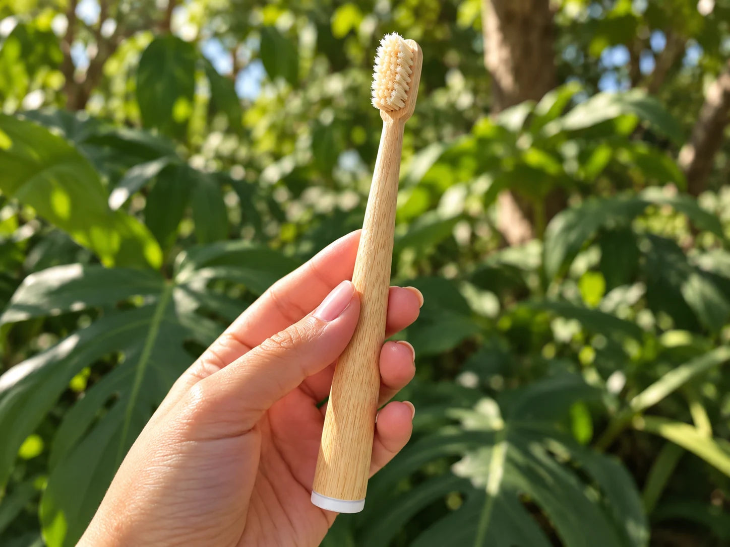 Mumzu bamboo and boar bristle toothbrush held in a hand outdoors